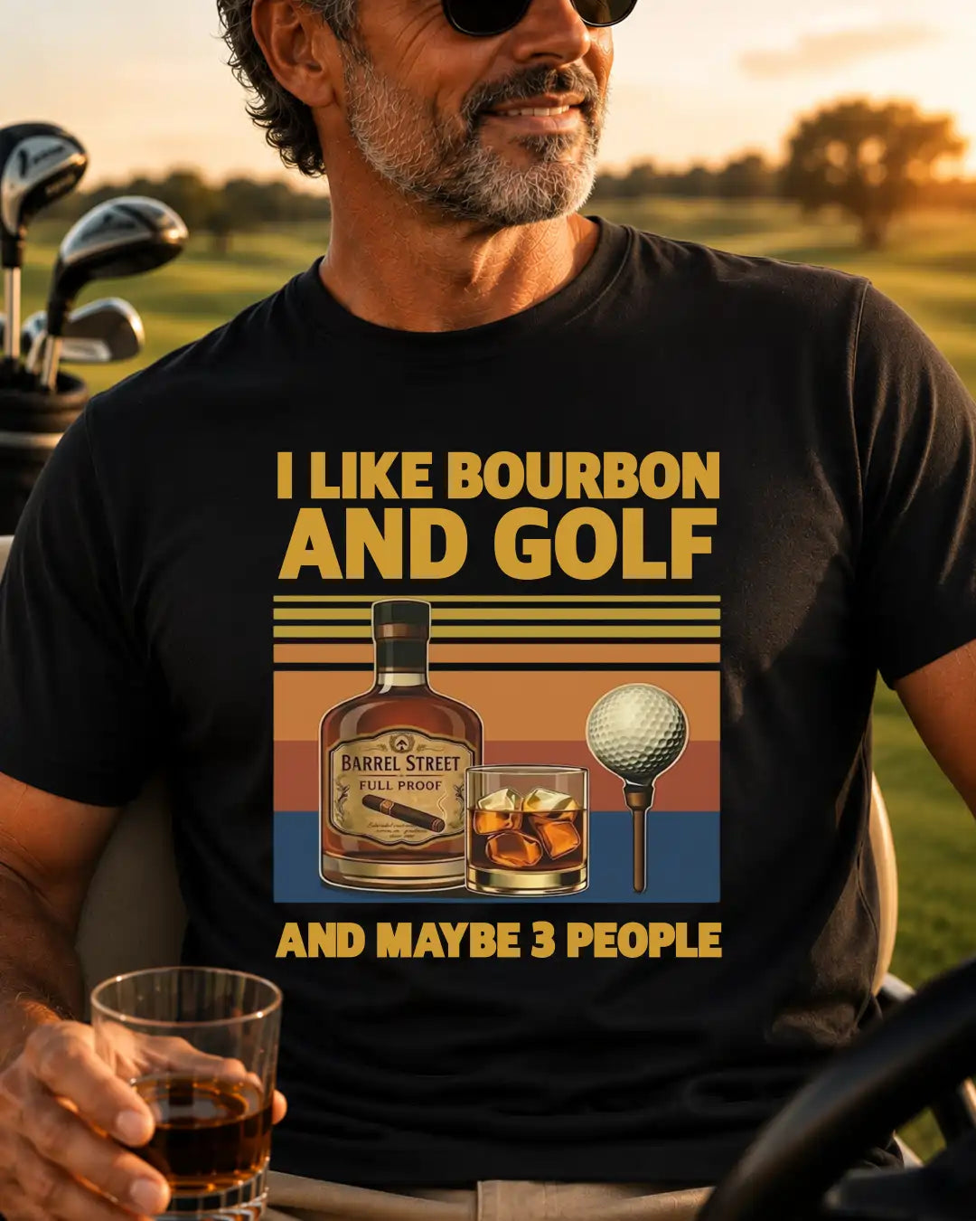 A man wearing a black graphic t-shirt with a vintage-style print that reads 'I LIKE BOURBON AND GOLF AND MAYBE 3 PEOPLE' alongside illustrations of a whiskey bottle, a glass of whiskey, a golf ball on a tee, and a sunset background.