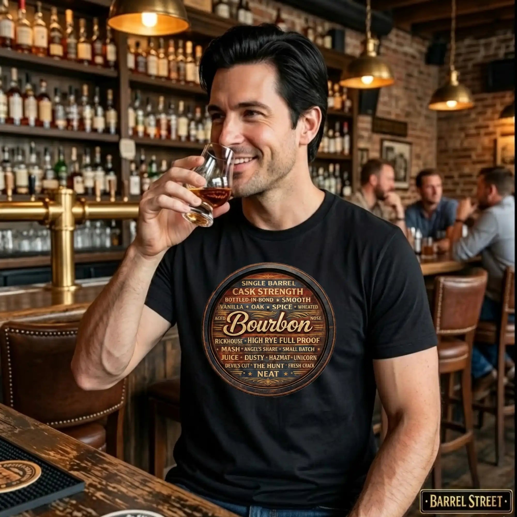 Man in a bar wearing a black t-shirt with 'Barrel Street' bourbon design, holding a glass of bourbon.