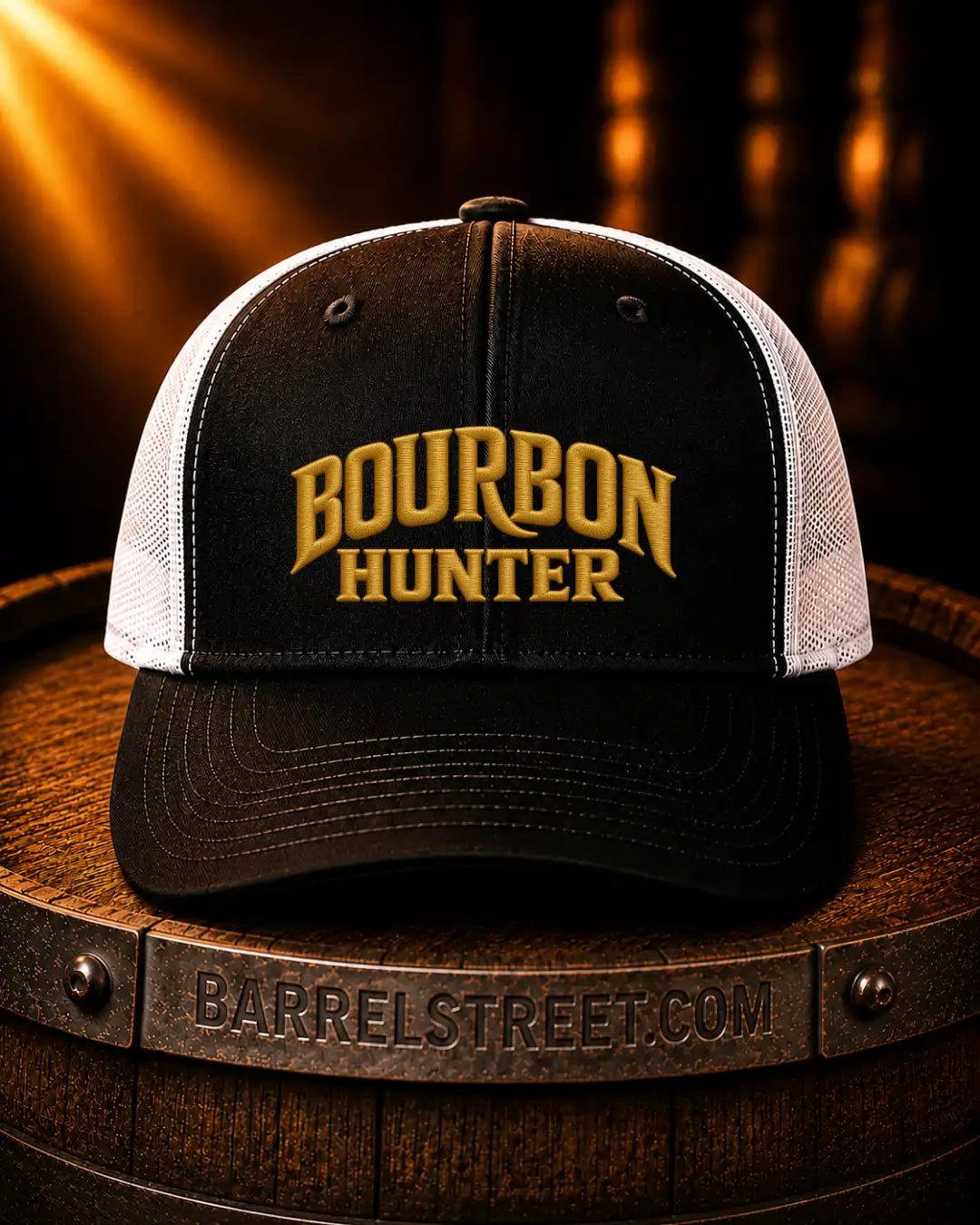 A black and white trucker cap with 'BOURBON HUNTER' embroidered in gold on the front, resting on a wooden barrel with a Barrelstreet.com band visible in the foreground.