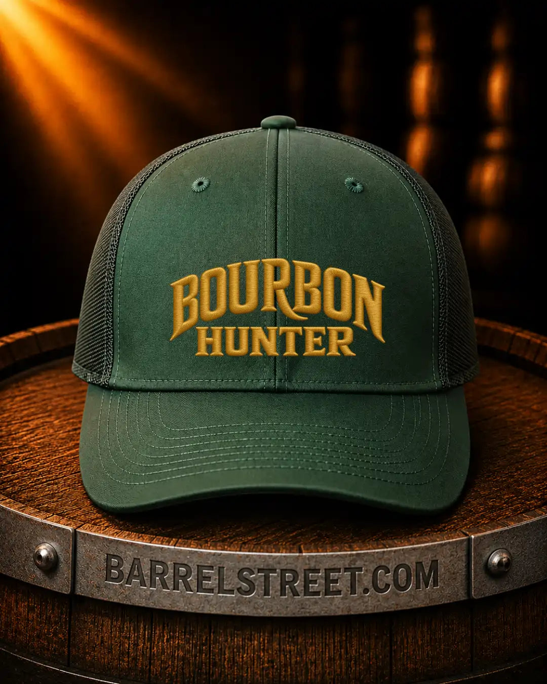 A dark green trucker-style baseball cap with 'BOURBON HUNTER' embroidered in gold on the front, displayed on a wooden barrel with a Barrelstreet.com logo visible on the metal band.