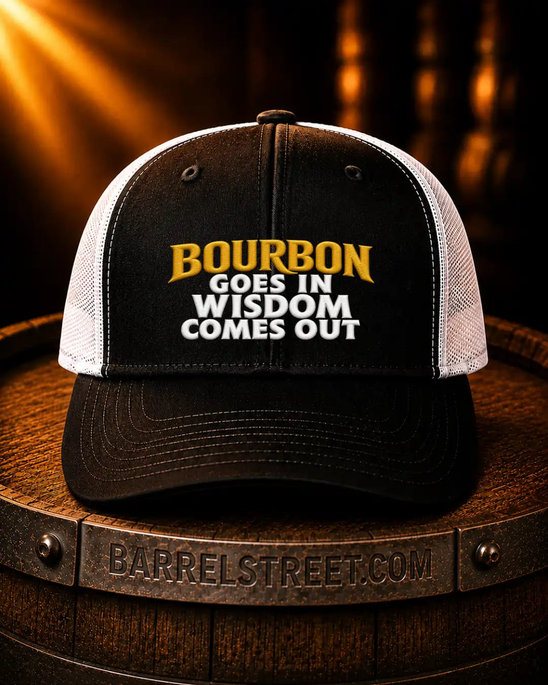 A black and white trucker cap with the text 'BOURBON GOES IN WISDOM COMES OUT' in yellow and white on the front, displayed on a wooden barrel with a Barrelstreet.com logo.