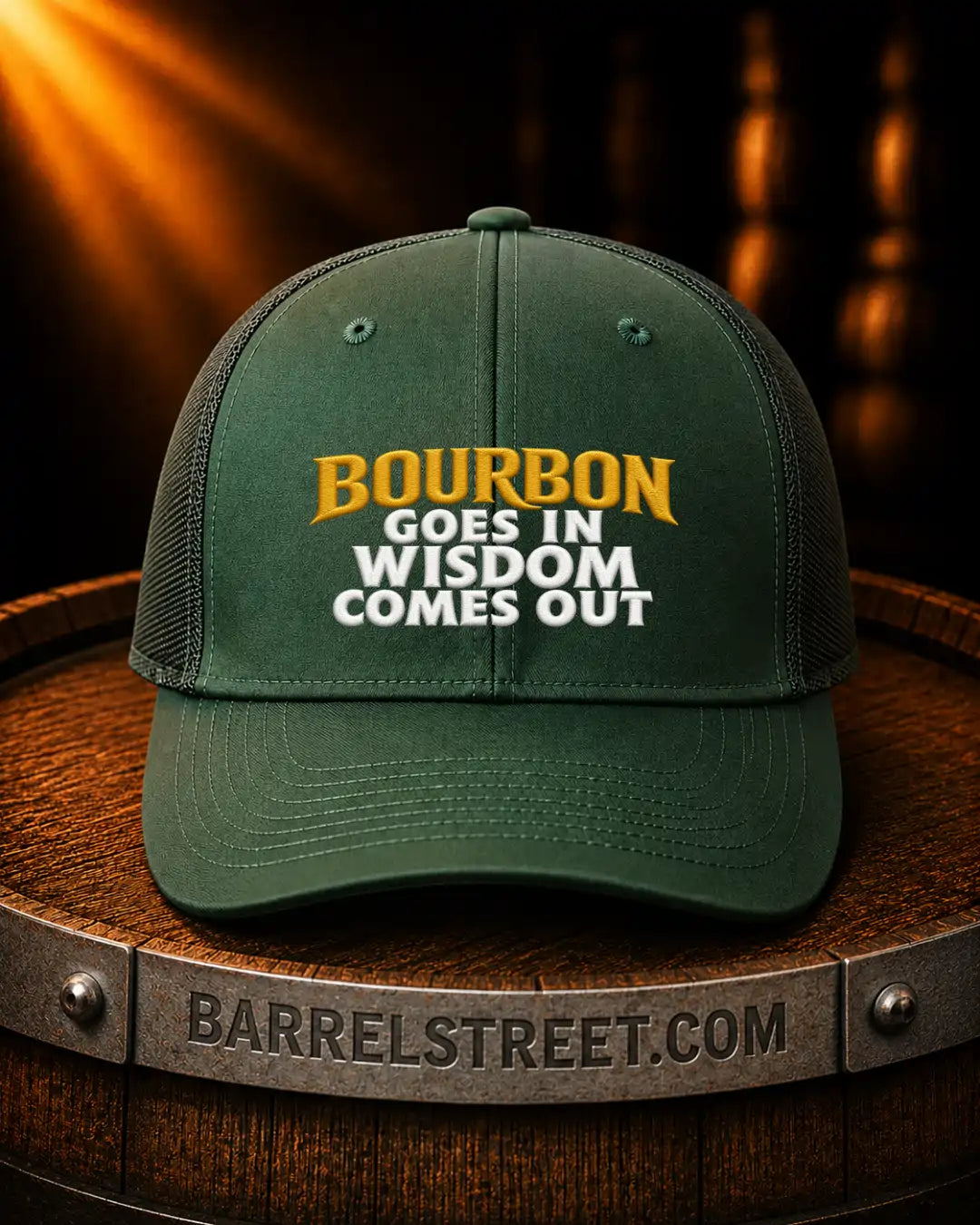 A dark green trucker-style cap with the embroidered text 'BOURBON GOES IN WISDOM COMES OUT' in yellow and white, displayed on a wooden barrel with a Barrelstreet.com logo.