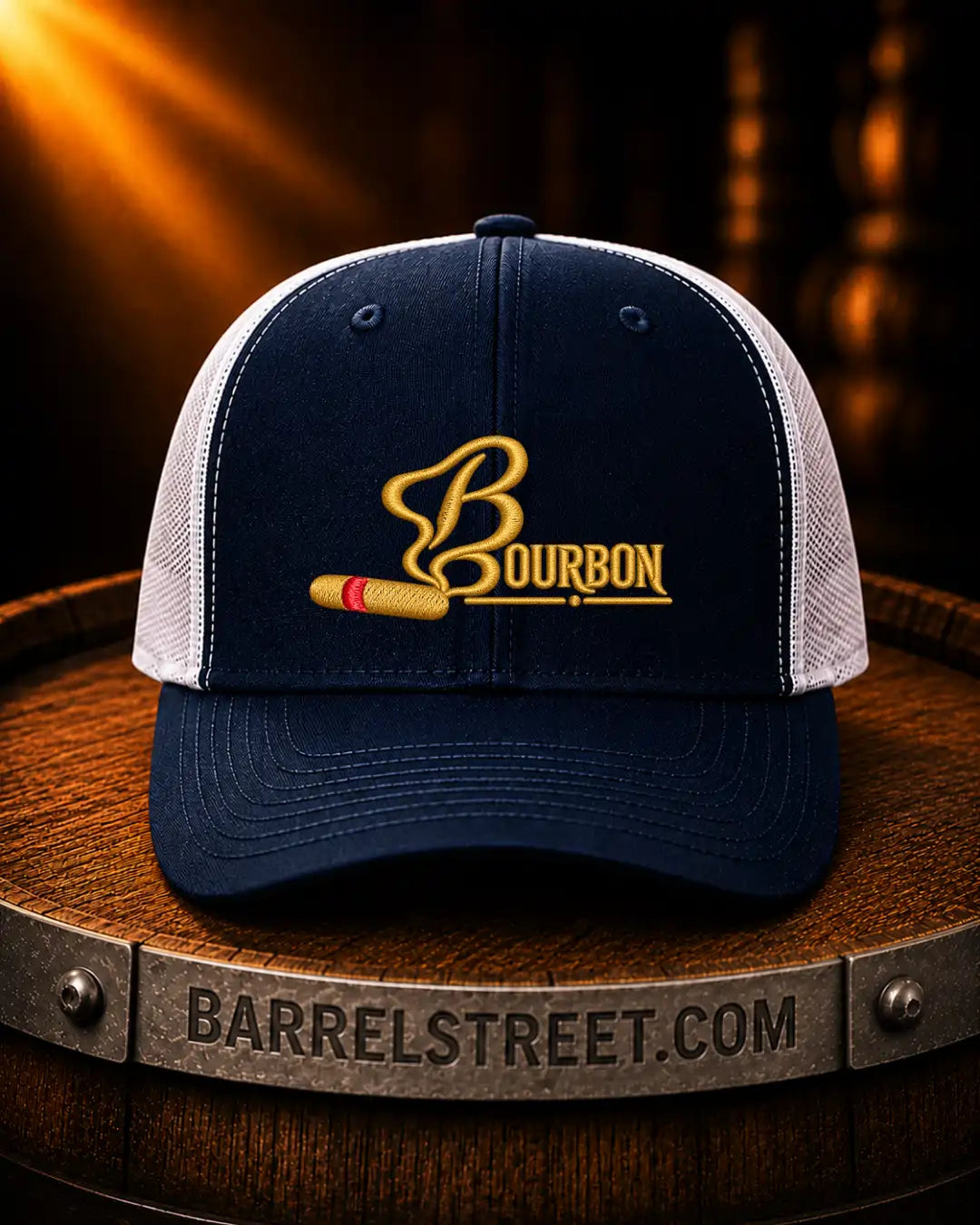 A navy and white trucker cap with a gold embroidered Bourbon logo and a cigar graphic, displayed on a wooden barrel with a Barrelstreet.com banner in the foreground.