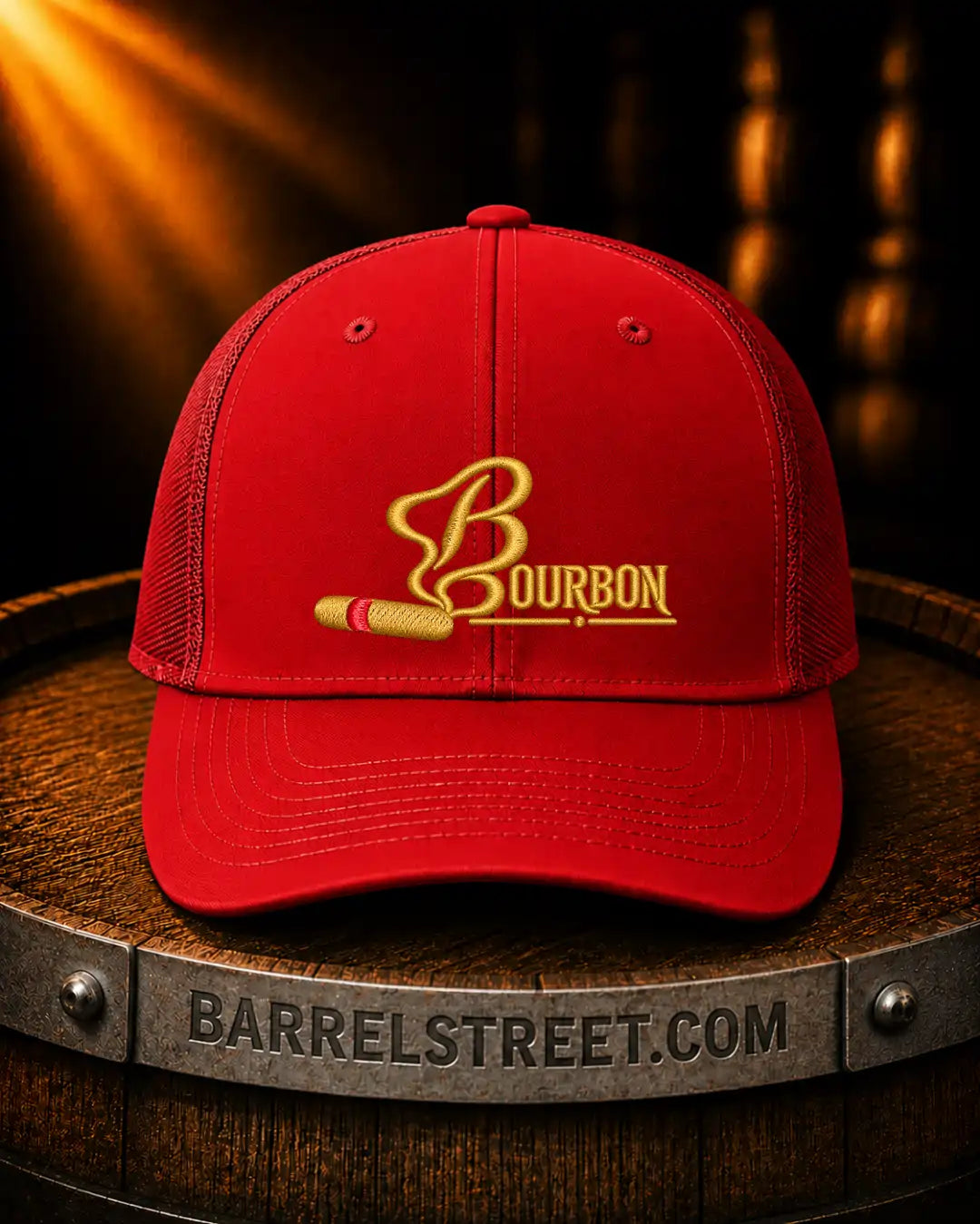 A red trucker-style cap with a gold embroidered Bourbon logo and a cigar graphic, displayed on a wooden barrel with warm dramatic lighting.