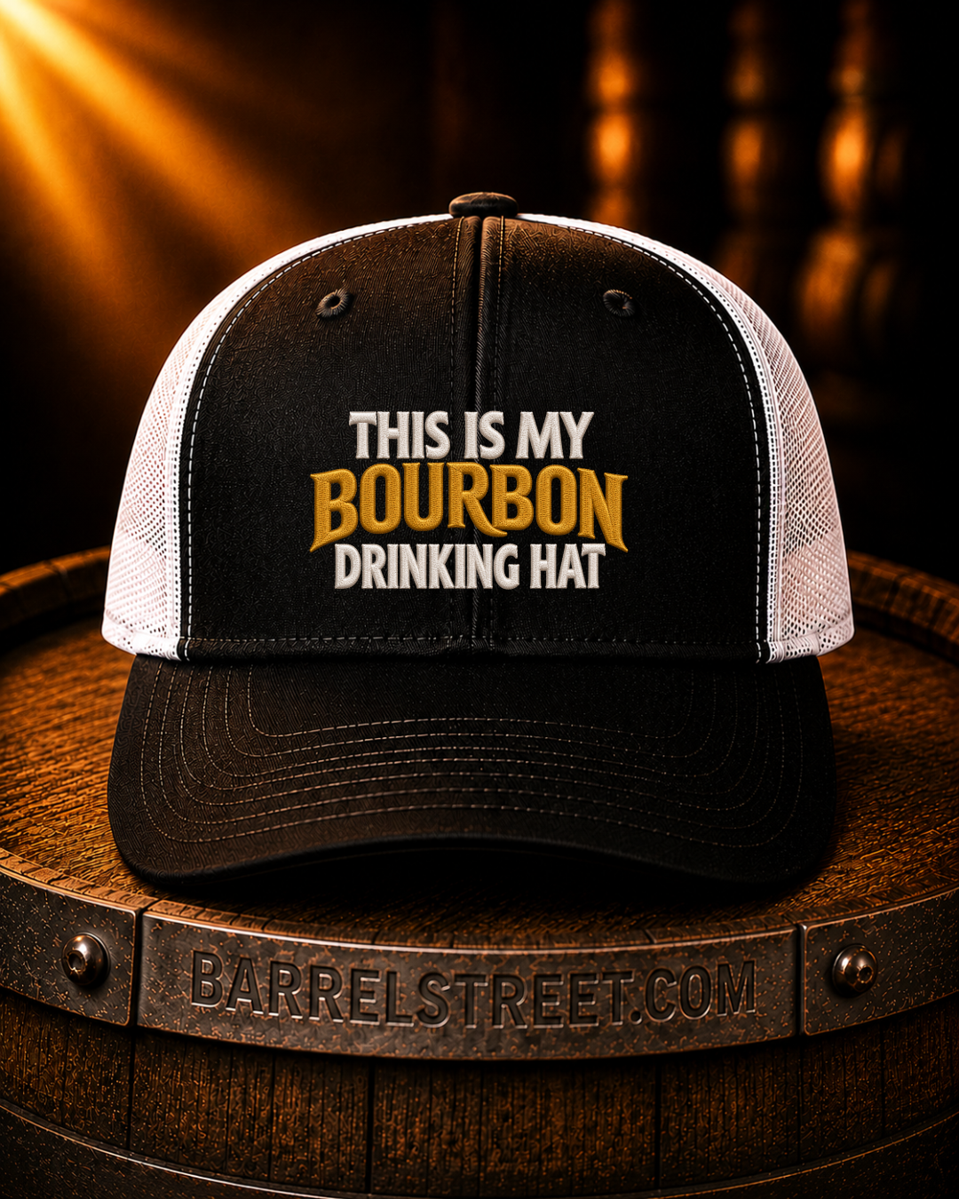 A black and white trucker hat with the text 'THIS IS MY BOURBON DRINKING HAT' on the front, displayed on a wooden barrel. The barrel has 'BARRELSTREET.