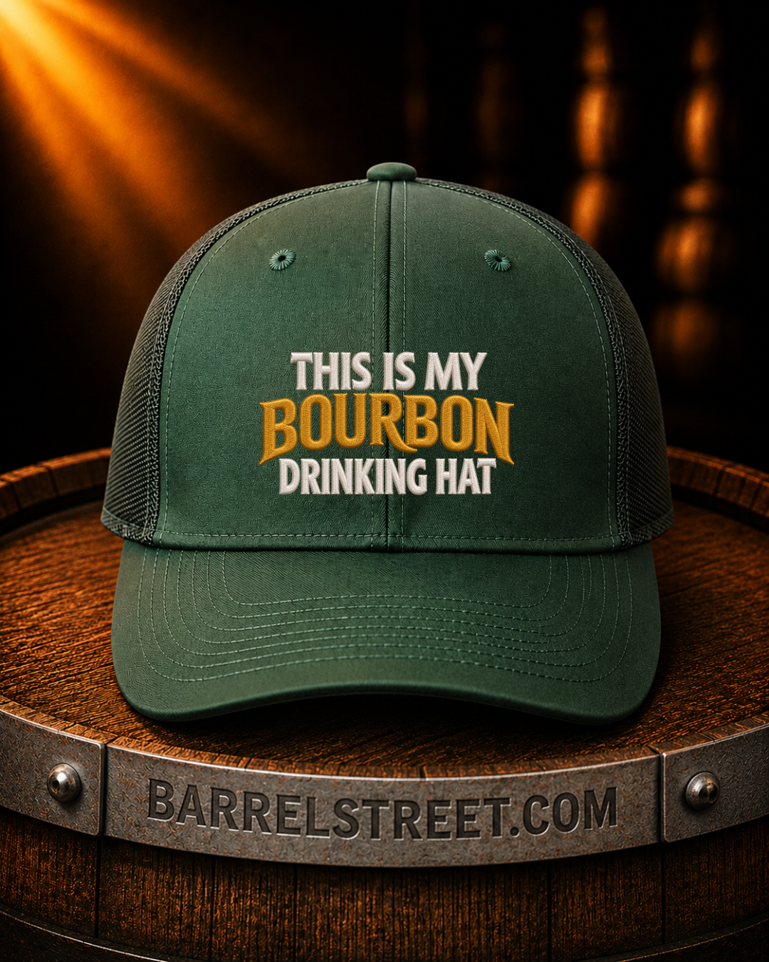 A dark green trucker-style cap with the text 'THIS IS MY BOURBON DRINKING HAT' on the front, displayed on a wooden barrel with a warm, moody background.