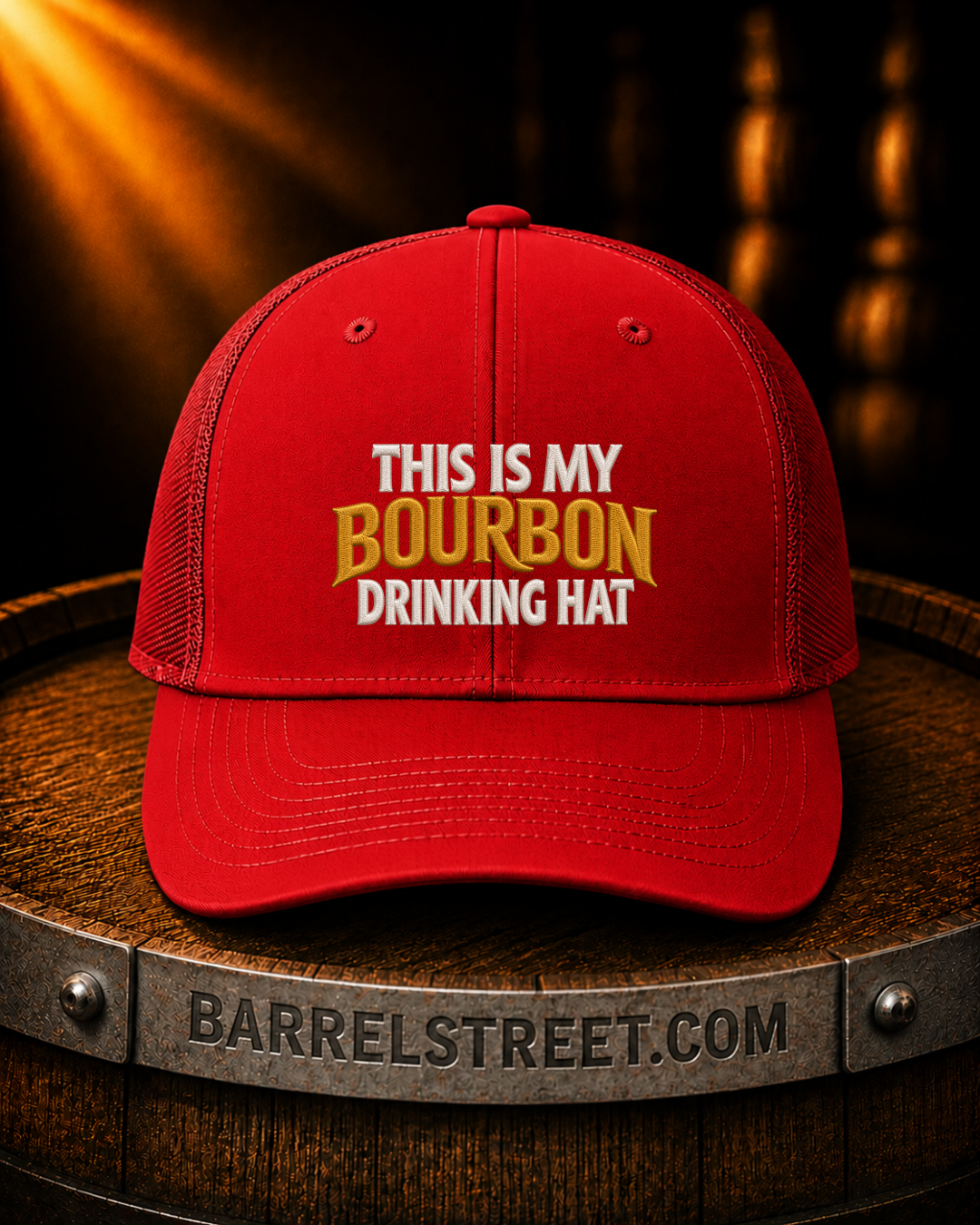 A red trucker-style cap with the text 'THIS IS MY BOURBON DRINKING HAT' in white and gold lettering, displayed on a wooden barrel. The barrel has 'BARRELSTREET.
