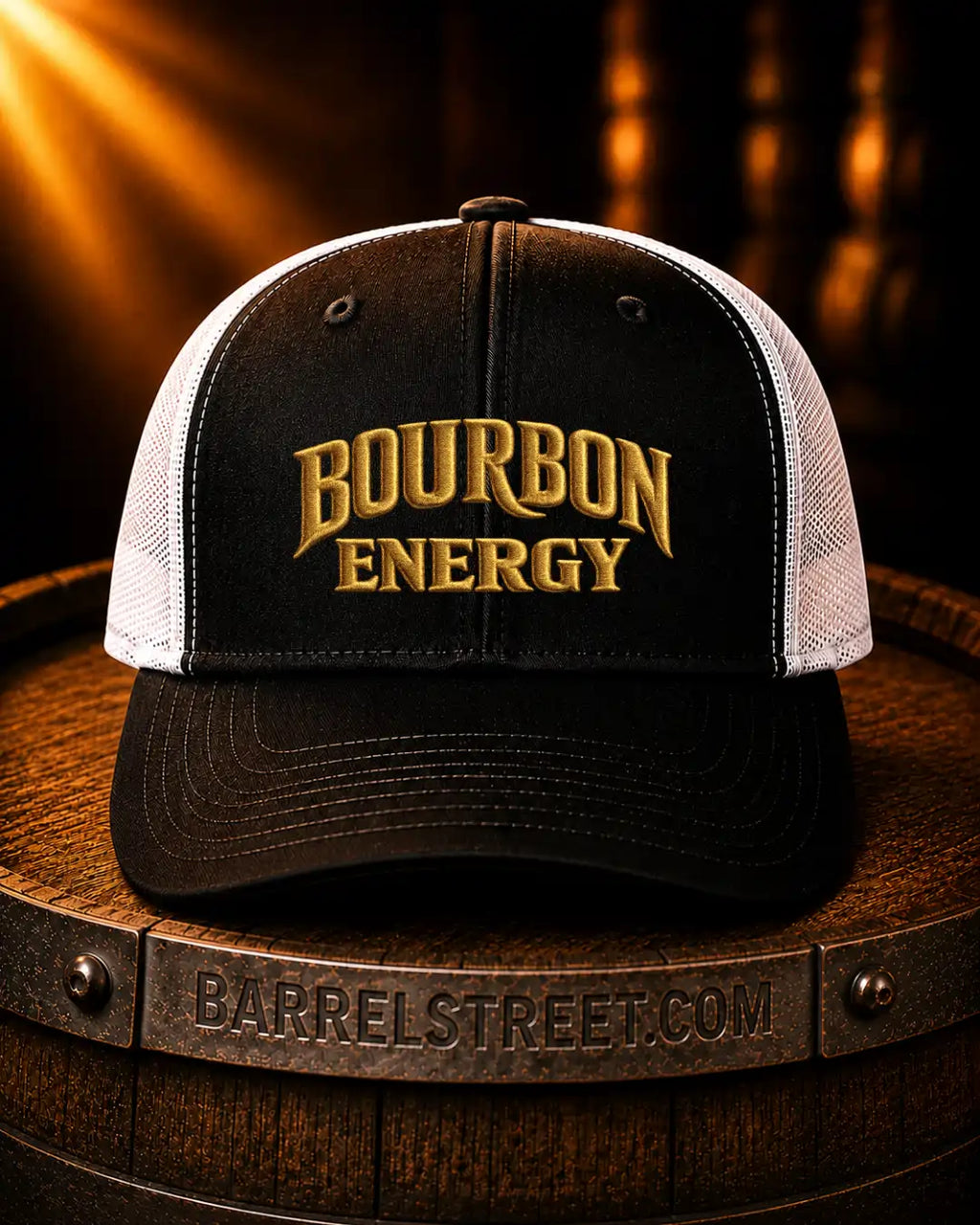 A black and white trucker hat with 'BOURBON ENERGY' embroidered in gold on the front, displayed on a wooden barrel with a dark, warm background.