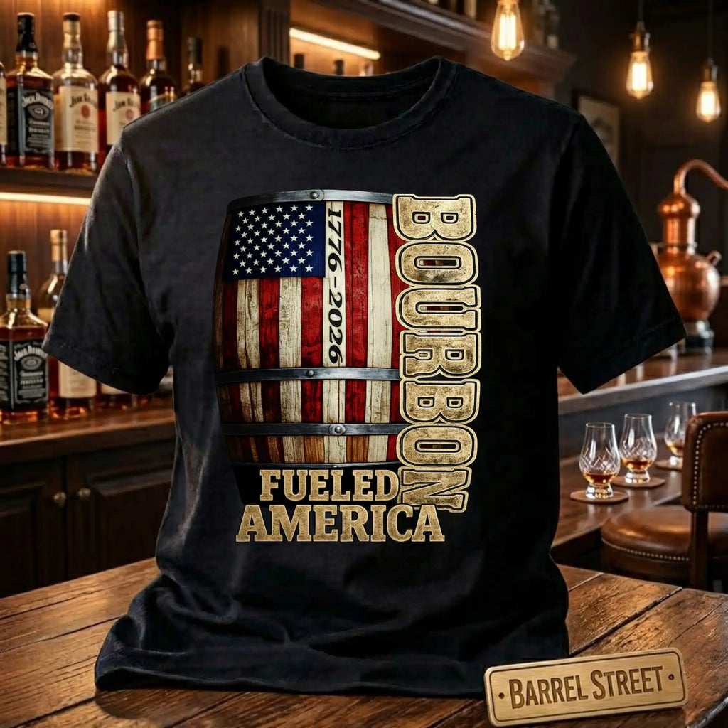 Black t-shirt with bourbon barrel design and 'Bourbon Fueled America' text in a bar setting.