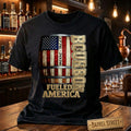 Black t-shirt with bourbon barrel design and 'Bourbon Fueled America' text in a bar setting.