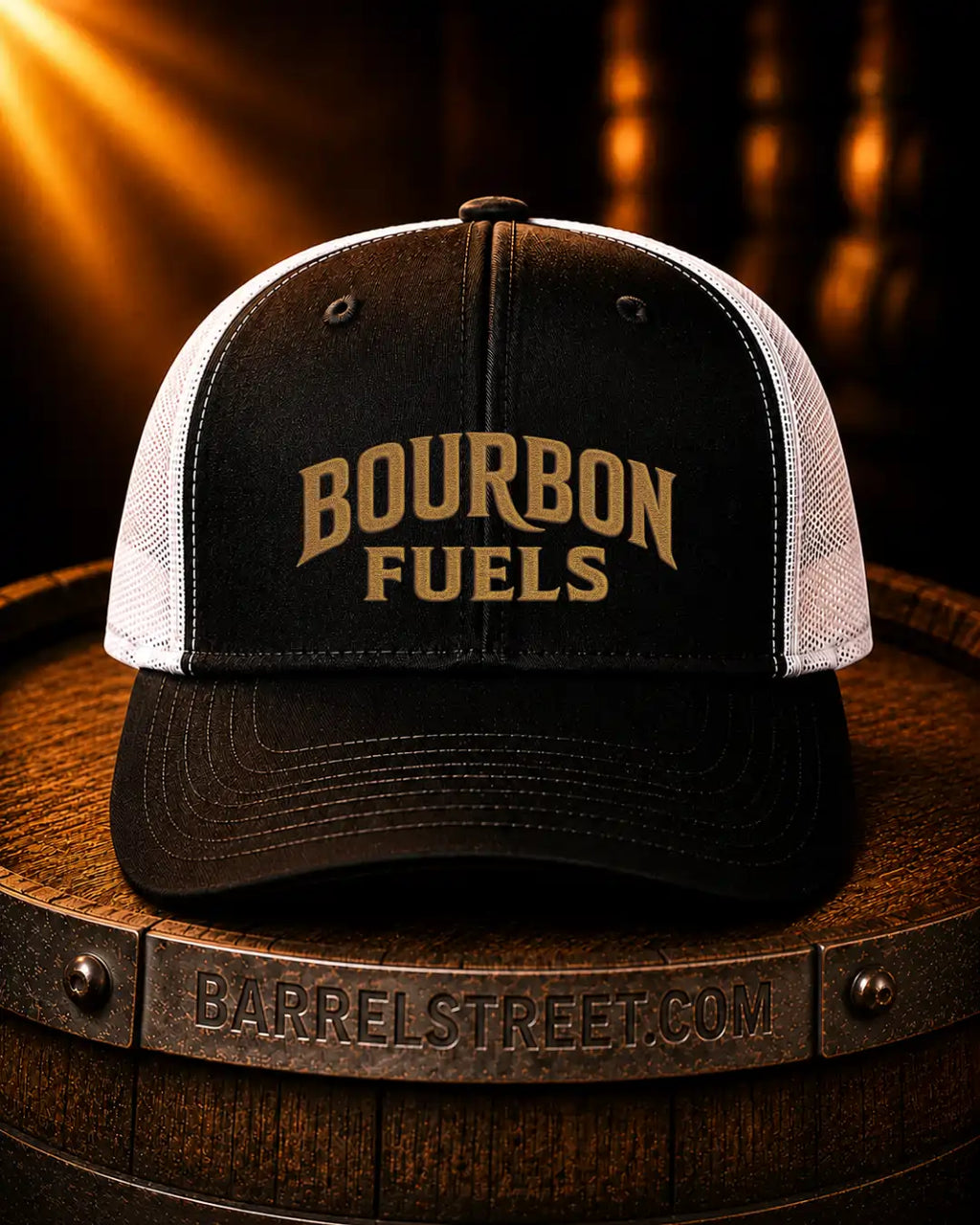 A black and white trucker hat with 'BOURBON FUELS' embroidered in gold on the front, resting on a wooden barrel with a Barrel Street branding band visible.