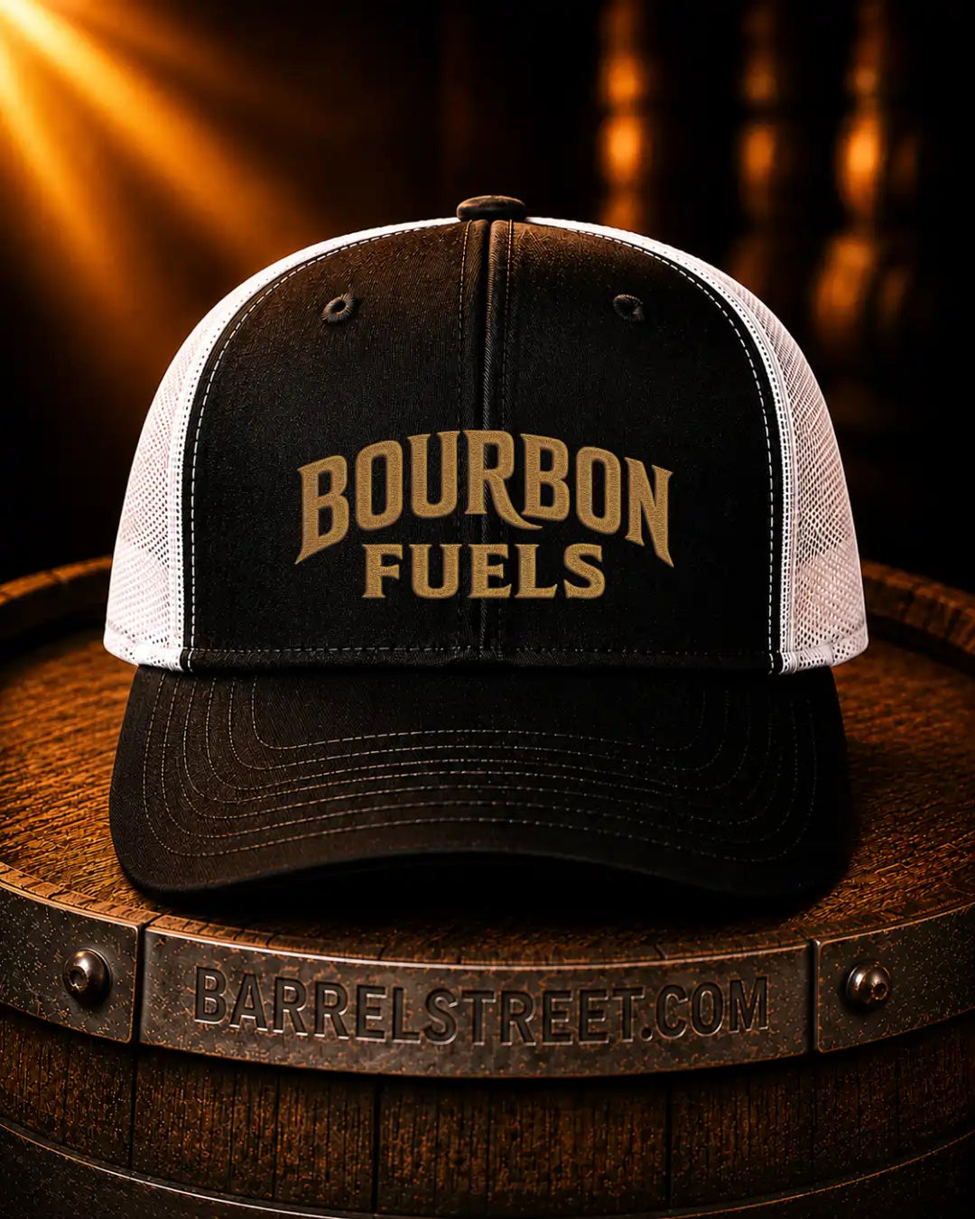 A black and white trucker hat with 'BOURBON FUELS' embroidered in gold on the front, resting on a wooden barrel with a Barrel Street branding band visible.