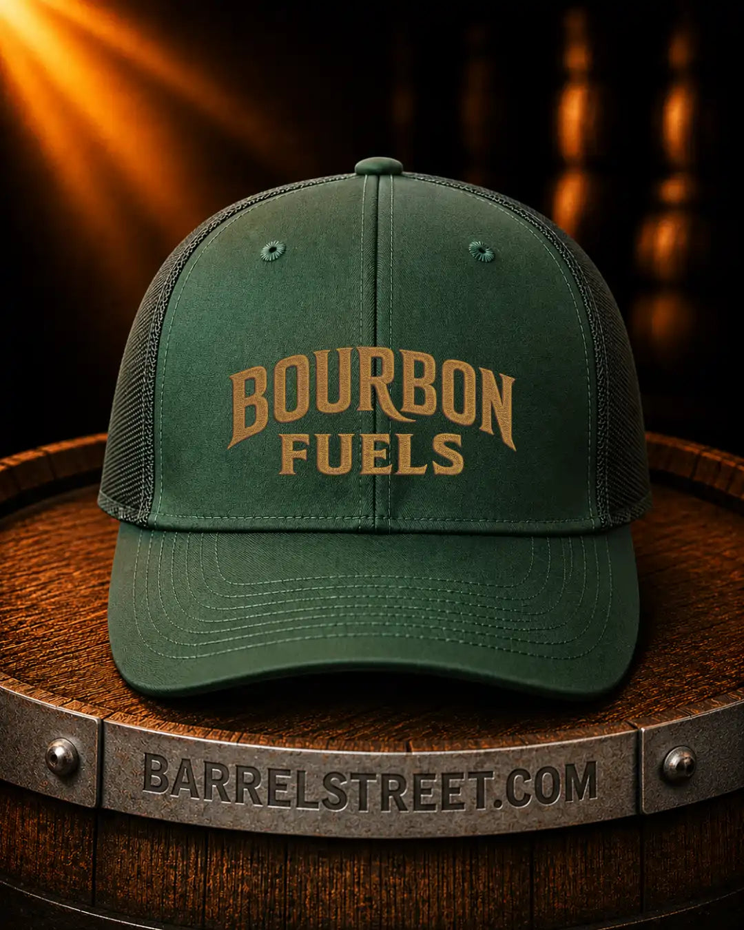 A dark green trucker-style cap with 'BOURBON FUELS' embroidered in tan on the front, displayed on a wooden barrel with a Barrelstreet.com logo visible on the metal band.