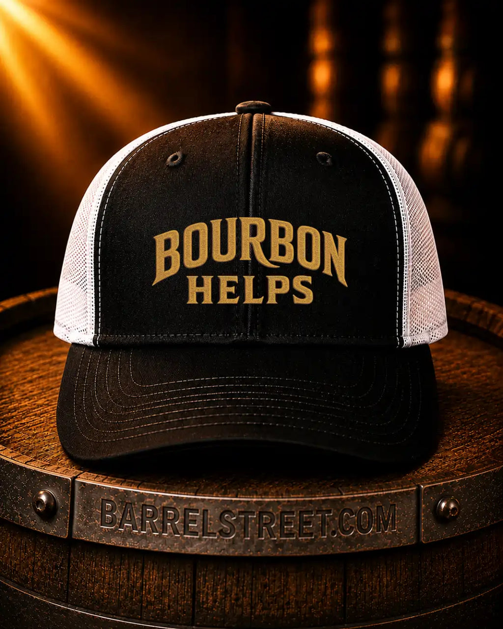 A black and white trucker hat with 'BOURBON HELPS' embroidered in gold on the front, displayed on a wooden barrel with a warm, dramatic background.