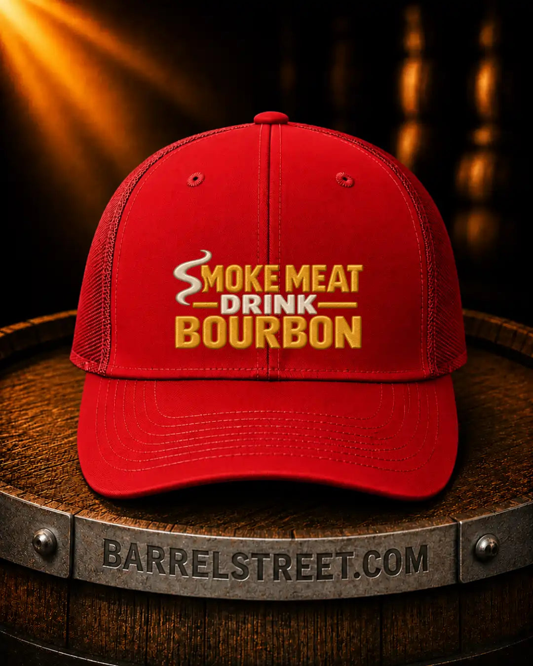 A red trucker-style cap with yellow embroidered text reading 'SMOKE MEAT DRINK BOURBON' sits on a wooden barrel. The barrel has 'BARRELSTREET.