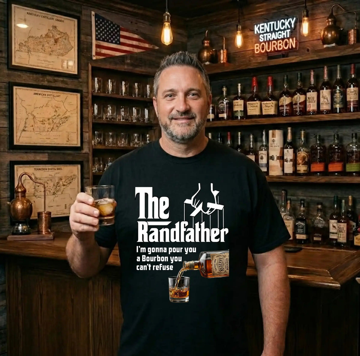 Man holding a glass of bourbon wearing a t-shirt with 'The Randfather' design in a bar setting.