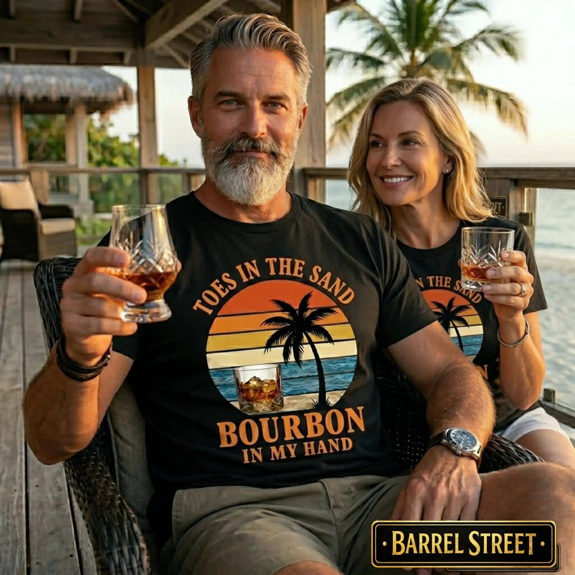 Man and woman sitting together, both holding glasses of bourbon, wearing 'Toes in the Sand Bourbon in My Hand' shirts.