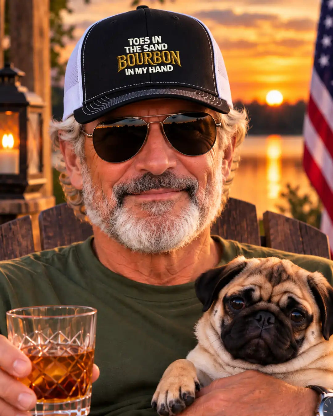 A man wearing a black and white trucker hat with the text 'TOES IN THE SAND BOURBON IN MY HAND' and sunglasses, sitting outdoors at sunset while holding a glass of whiskey and a pug dog.