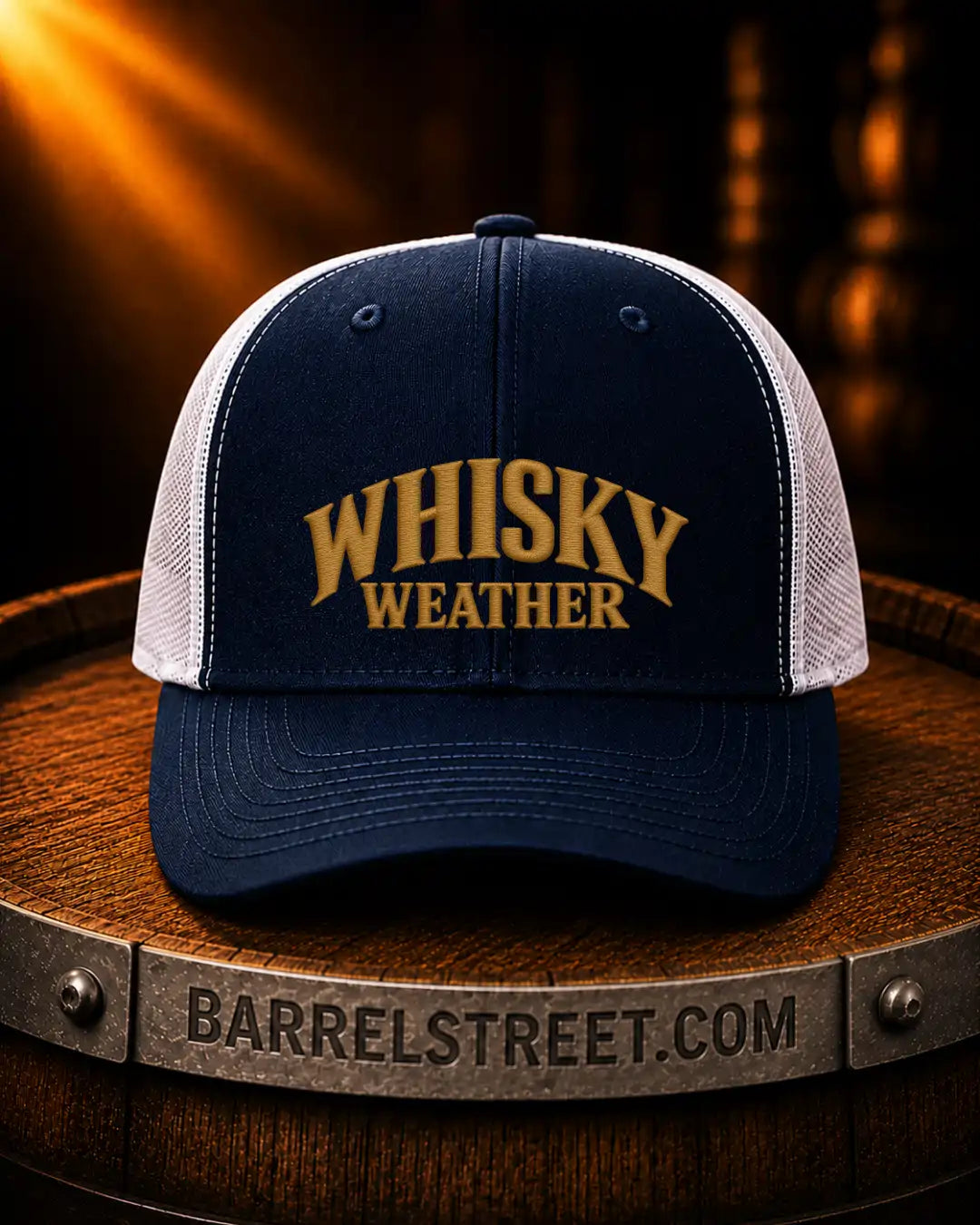 A navy blue and white trucker hat with 'WHISKY WEATHER' embroidered in gold on the front, displayed on a wooden barrel with a Barrelstreet.com logo visible on the metal band.