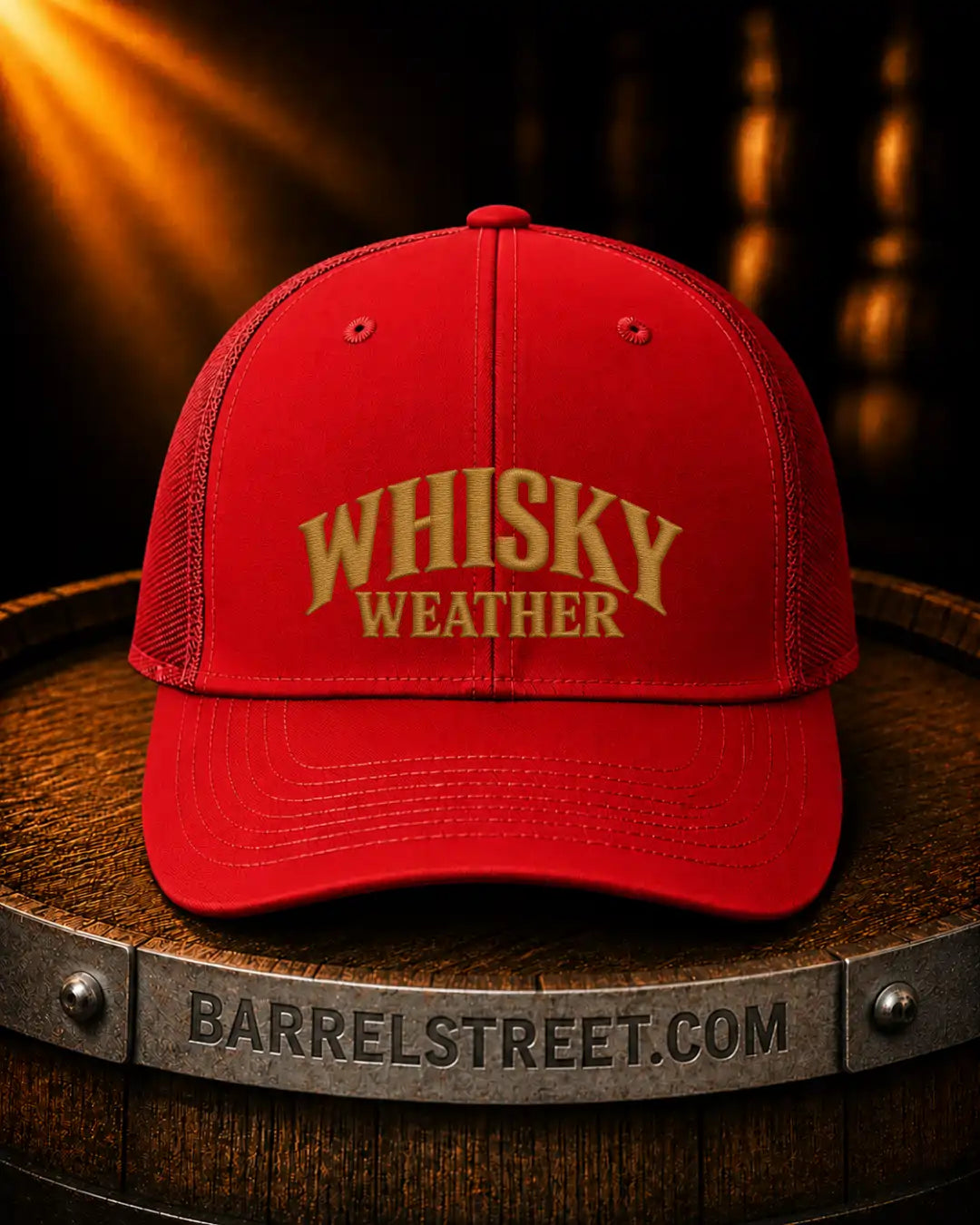 A red trucker-style cap with gold embroidered text reading 'WHISKY WEATHER' sits on a wooden barrel. The barrel has 'BARRELSTREET.