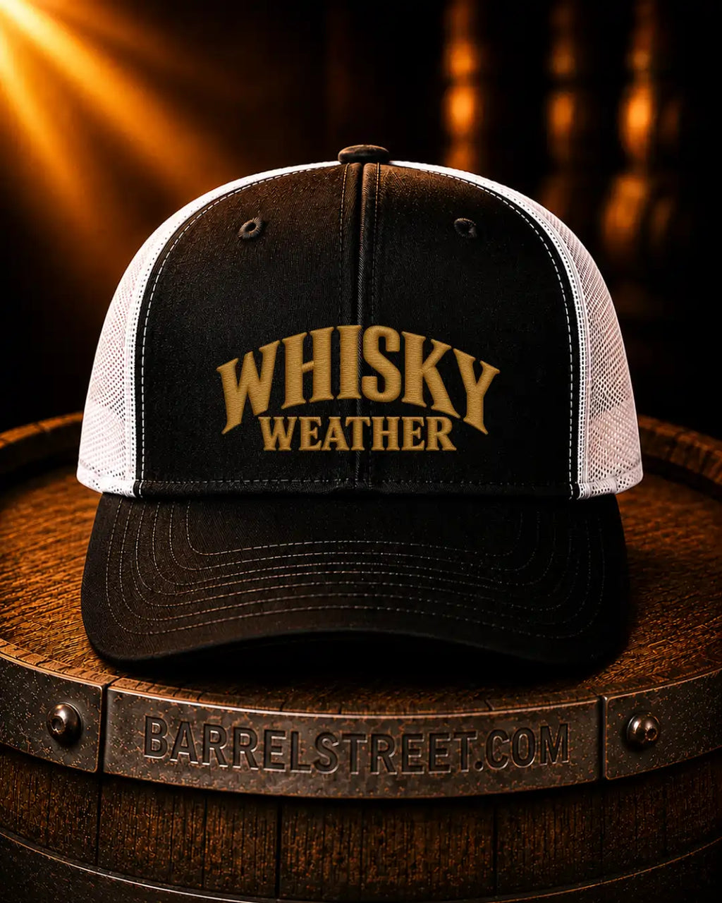 A black and white trucker hat with 'WHISKY WEATHER' embroidered in gold on the front, resting on a wooden barrel with a warm, dramatic background.